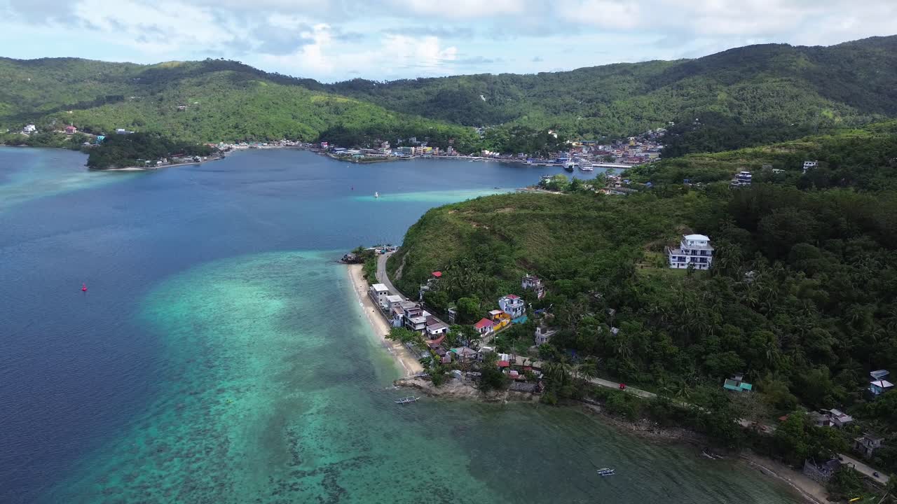 Vista aerea cinematografica della città e del porto di Romblon, nelle Filippine, che mostra la baia turchese, le case costiere, la spiaggia e le verdi colline sotto un cielo azzurro in una giornata tropicale e soleggiata, il tutto ripreso in 4K.