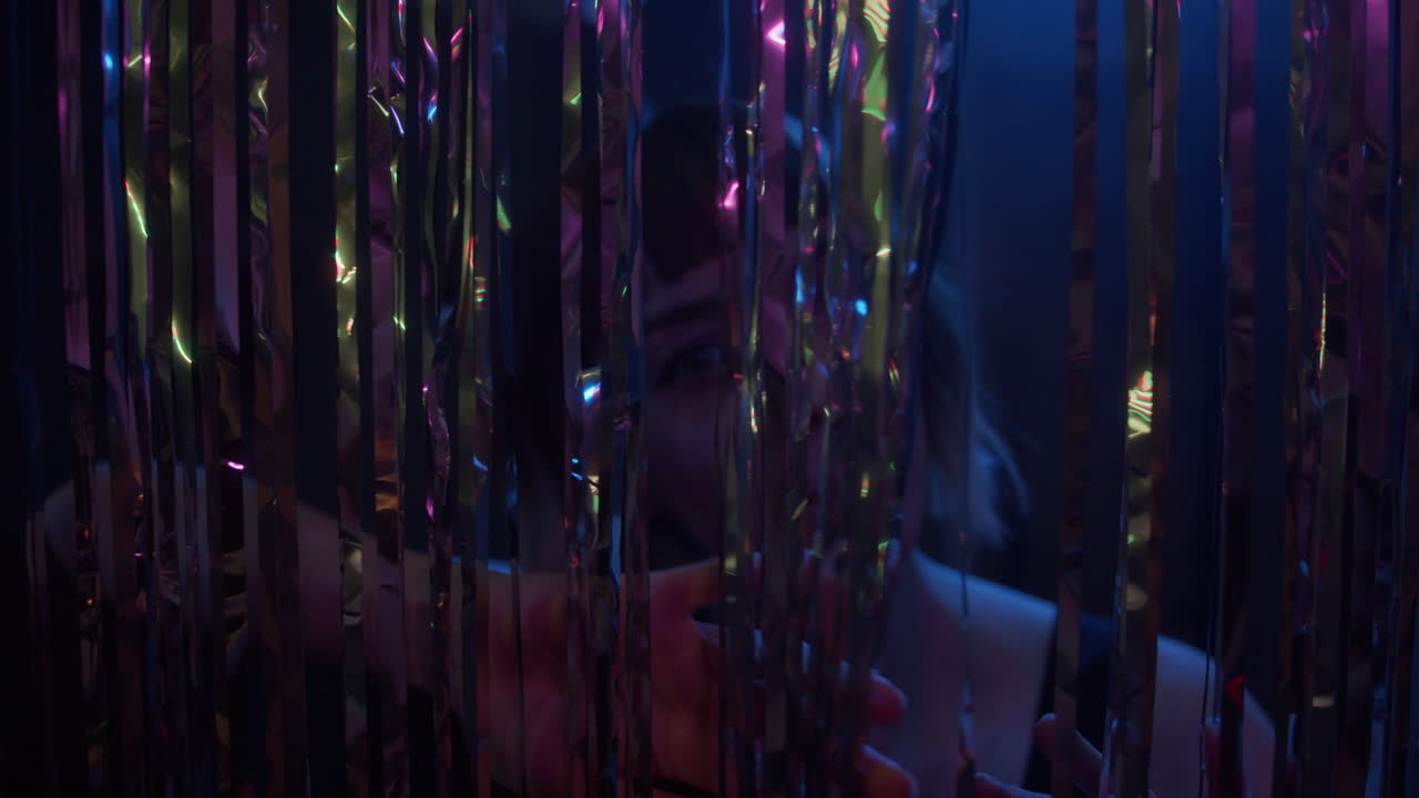 A young woman stares int the camera through glittering curtain