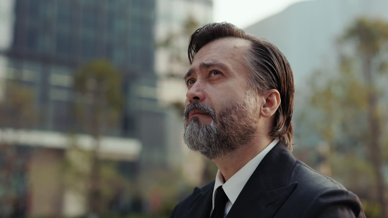 Thoughtful Bearded Businessman Looking Up in Urban Environment