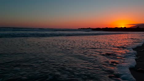 Tiro-De-Carro-Bajo-De-La-Playa-Durante-La-Puesta-De-Sol-Con-La-Luz-Del-Sol-Reflejándose-Bellamente-En-La-Arena-Y-Las-Olas-Que-Entran-En-La-Playa-Estatal-De-San-Buenaventura-En-Ventura,-California,-Ee.uu.