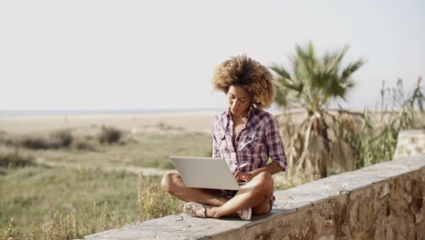 Mujer-Con-Computadora-Portátil-Sentada-En-La-Pared-De-Piedra