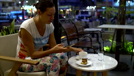 a woman in a cafe with a smartphone drinks coffee and eats a tiramisu cake