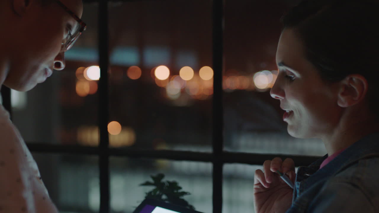 태블릿 컴퓨터를 사용하여 늦게 일하는 사업가 동료들이 연구 통계를 공유하고 화면에서 그래프 데이터를 논의하고 창의적인 여성들이 밤에 사무실에서 협력합니다.