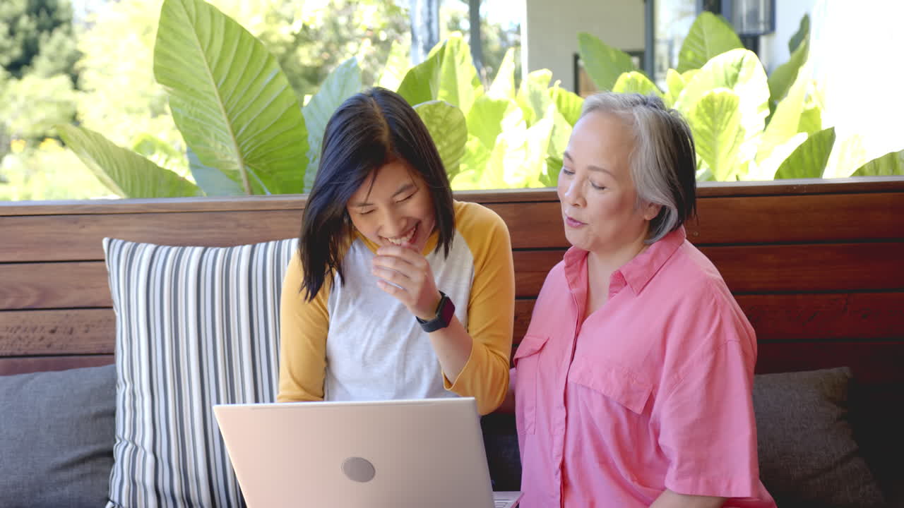 Using laptop, two women sitting on couch, focusing on screen together