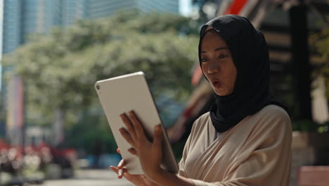 smiling young woman in hijab using a tablet outdoors