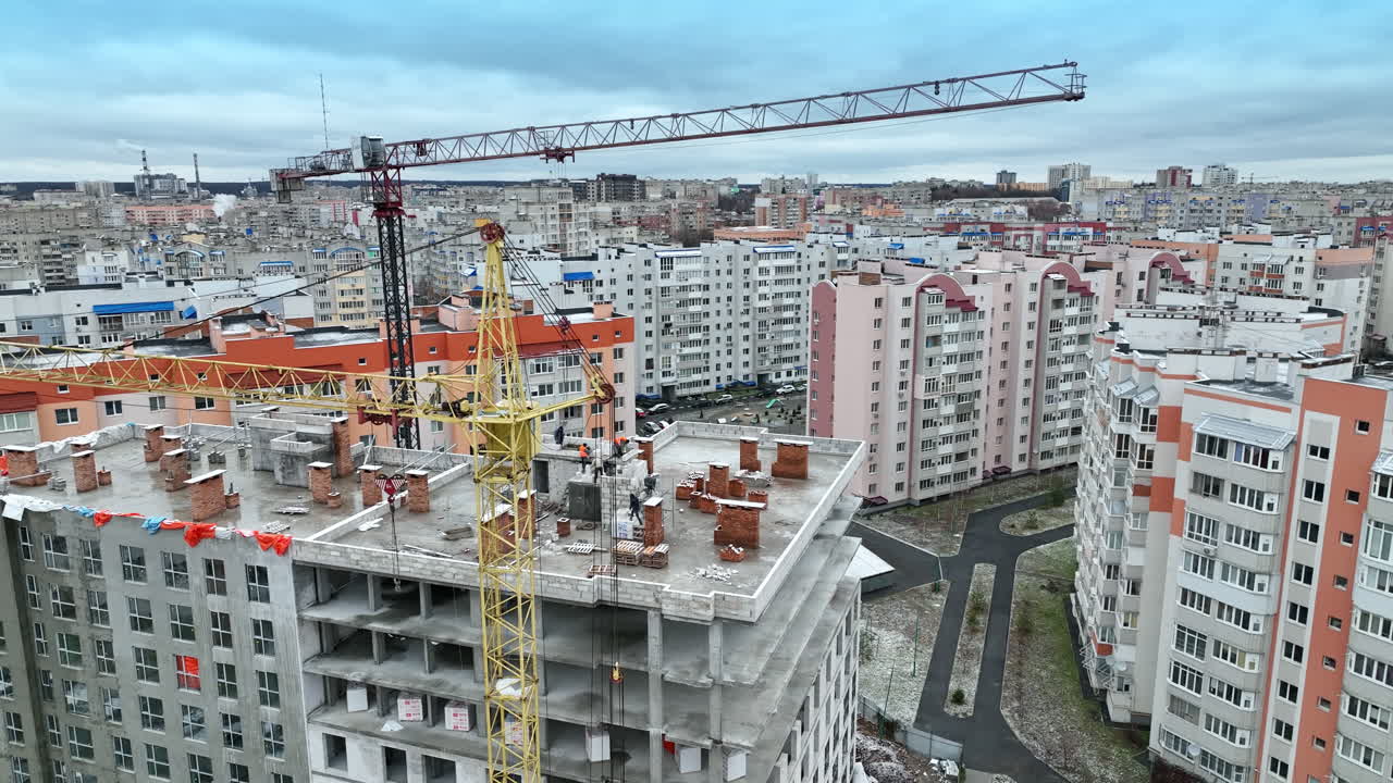 Builders working on the roof of the multi-storied house. High block of flats with construction crane beside. Circle movement footage.