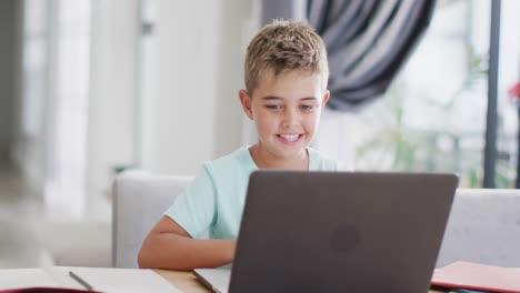 Glücklicher-Kaukasischer-Junge,-Der-Am-Tisch-Sitzt-Und-Laptop-Für-Online-Unterricht-Benutzt,-Zeitlupe