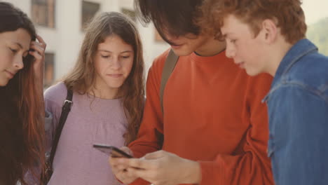 a group of teenagers with two girls and two boys watching something on the screen of a mobile phone