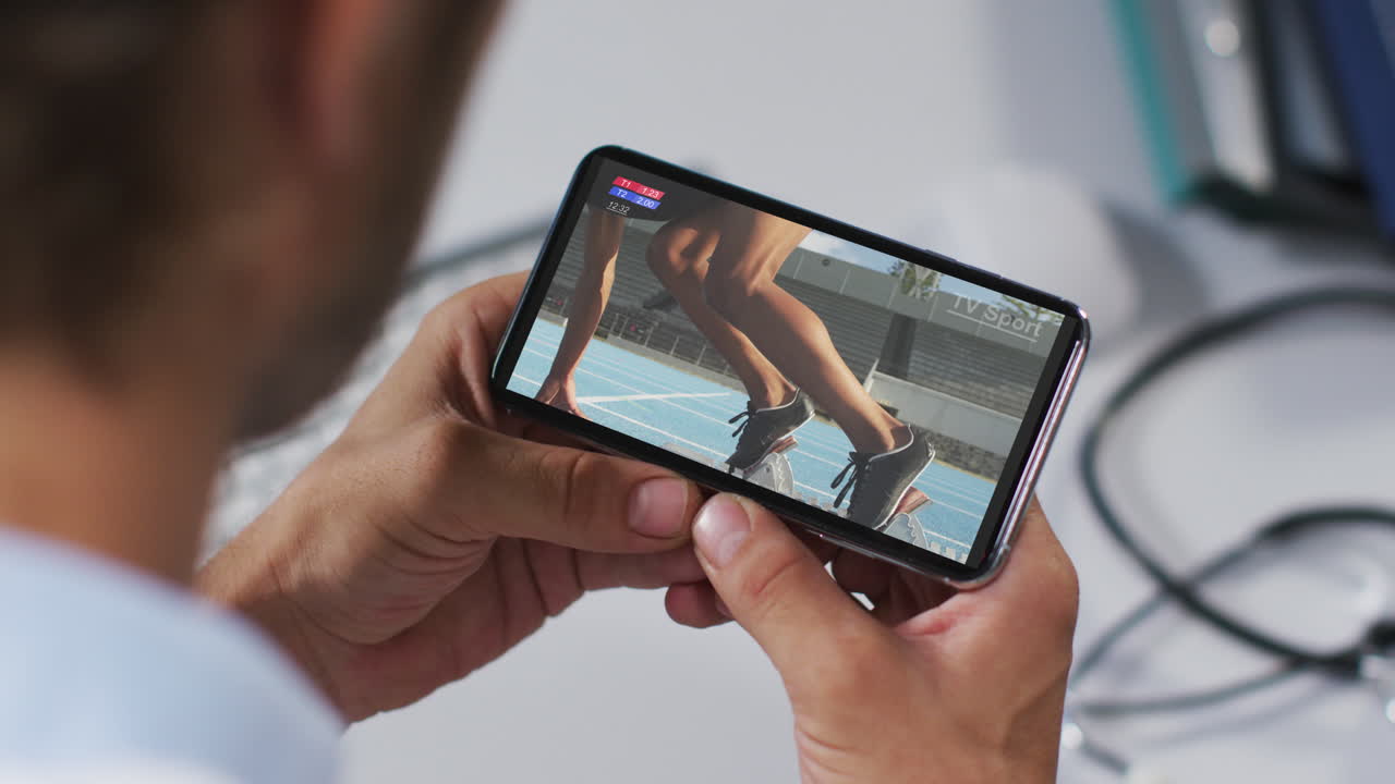 compuesto de un médico masculino viendo un evento de atletismo en un teléfono inteligente
