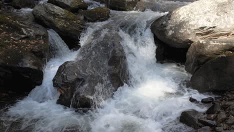 mountain stream splashes over river rocks in small waterfall, slow motion