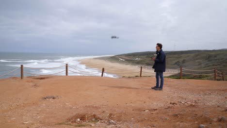 Ein-Junger-Reisender-Startet-Und-Fliegt-Eine-Drohne-An-Einem-Malerischen-Strand-Von-Nazare-In-Portugal