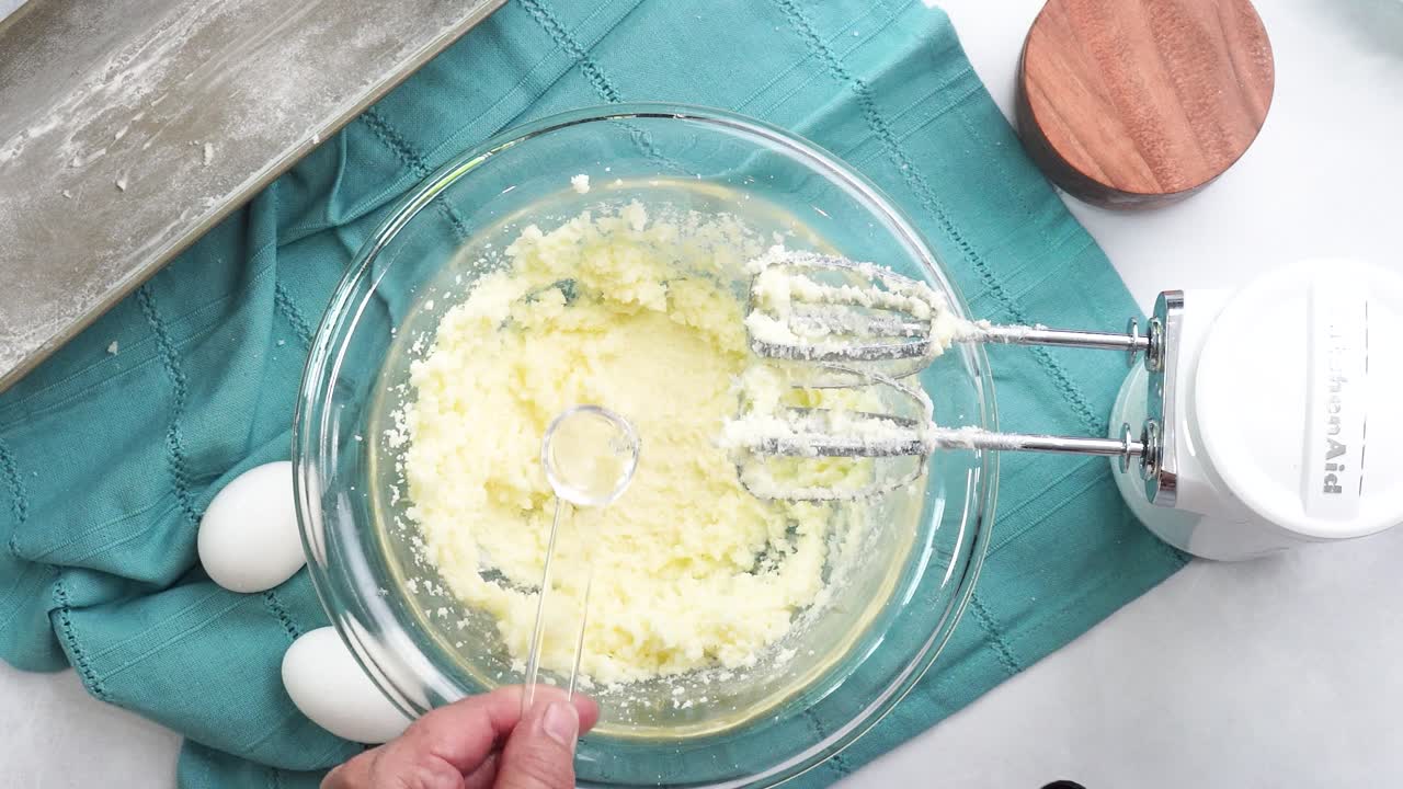 Making a dessert called Red Raspberry Tea Cake made with fresh berries and vanilla buttercream frosting. Great for Tea Parties. Adding almond extract to the mixing bowl and combining the ingredients