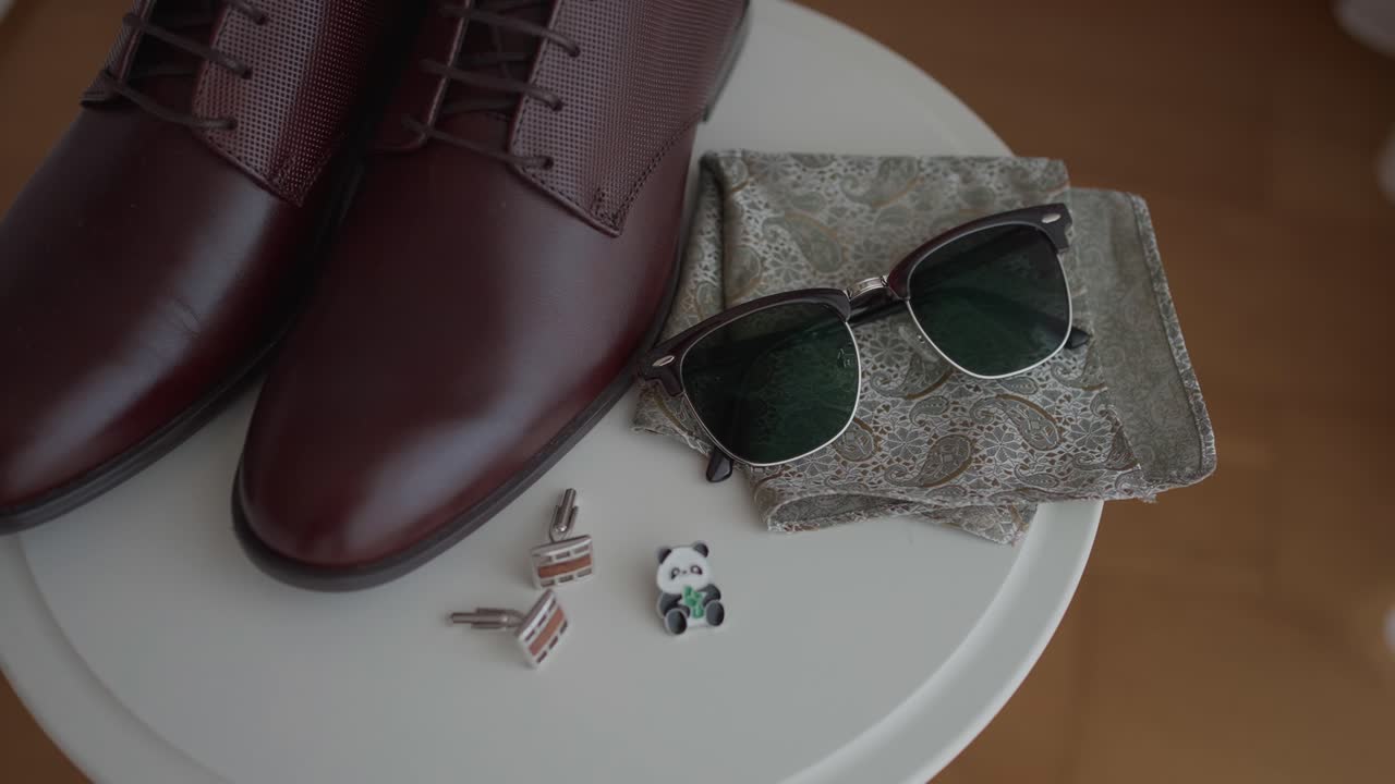 광택이 나는 갈색 가죽 신발, 선글라스, 패턴 포켓 스퀘어, 커프스 단추의 클로즈업