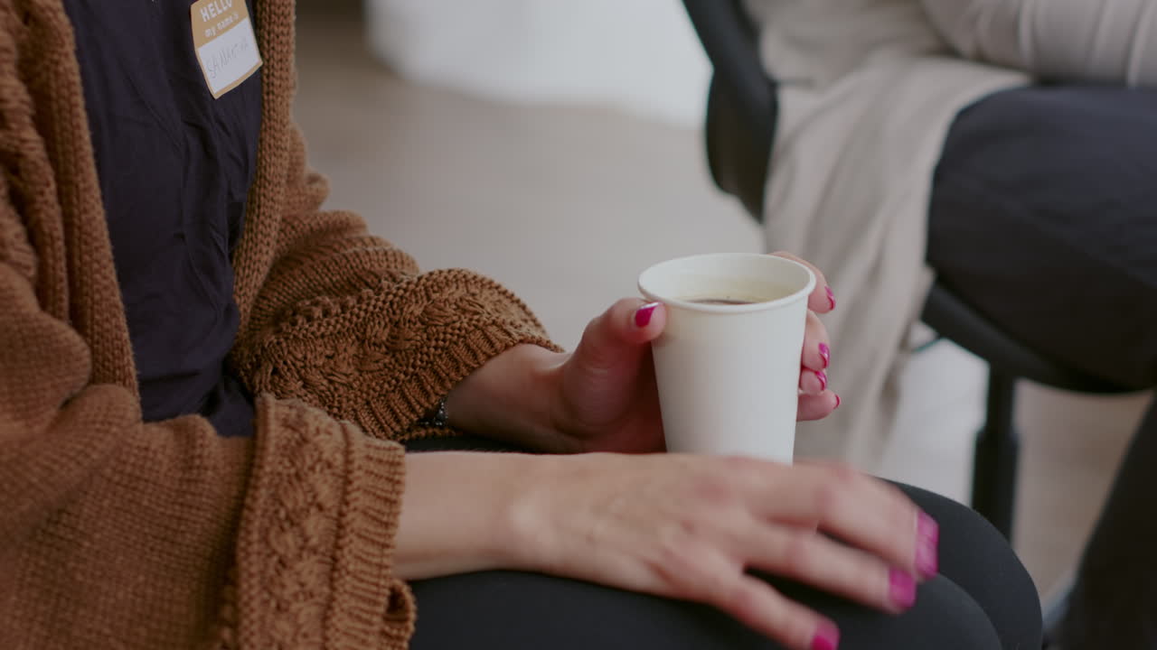 Close up of nervous woman holding cup of coffee and trembling at aa therapy meeting