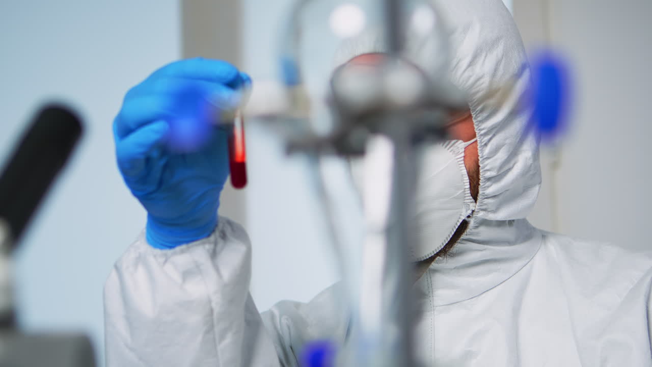 Tecnico di laboratorio in tuta DPI che analizza un campione di sangue