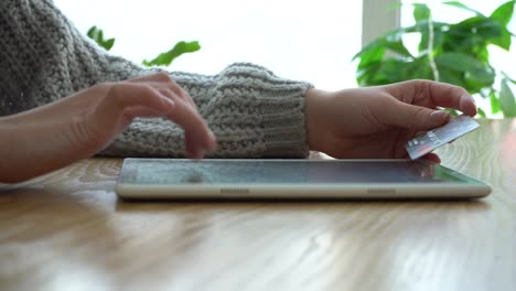 Girl holding a credit card layout and using a tablet computer while sitting in a coffee shop