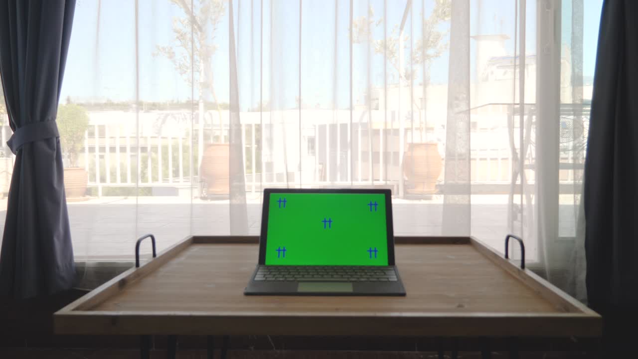 Chroma key green screen of laptop computer set on wooden table in apartment. Window curtains on background. Working from home.