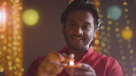 man celebrating festival of diwali holding lit diya oil lamp towards camera 1