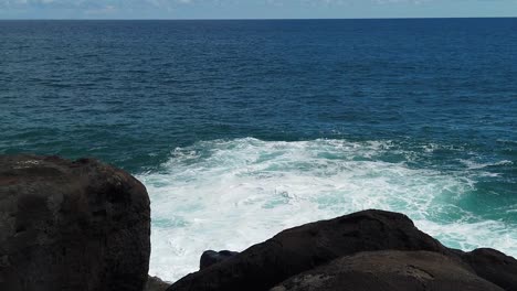 hd slow motion hawaii kauai static of ocean waves building and crashing with some ocean spray with big lava rocks in foreground and ocean horizon near top of frame