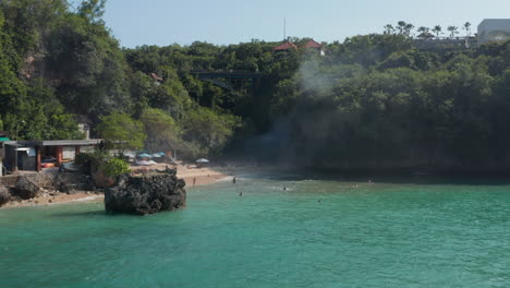 People-swimming-on-a-hidden-tropical-sand-beach-surrounded-by-rocky-cliffs.-Tourists-relaxing-on-a-sandy-beach-in-Bali,-Indonesia