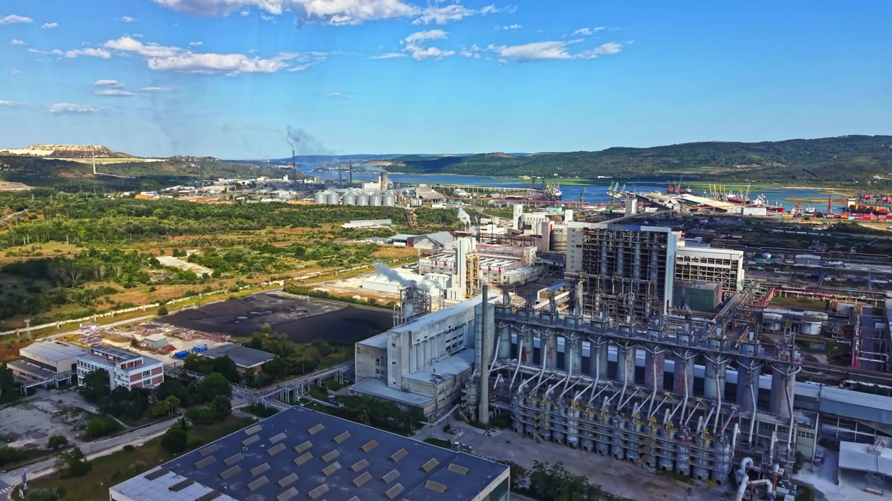 Industrial site with factories and machinery located near water body and greenery under blue sky