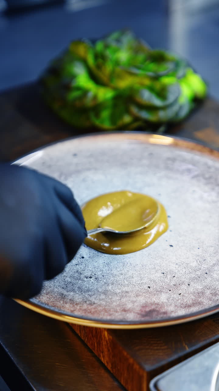 A cook in black latex gloves puts some sauce on the plate. The thick gravy is spread by the plate with a spoon. Close up. Vertical video.