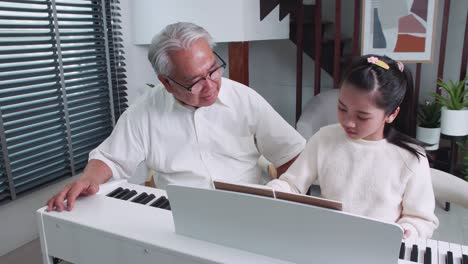 grandfather is teaching little granddaughter to play the piano at home.