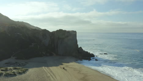 Toma-Aérea-De-Una-Playa-Vacía-Durante-El-Día-Con-Una-Montaña-Rocosa-Al-Costado