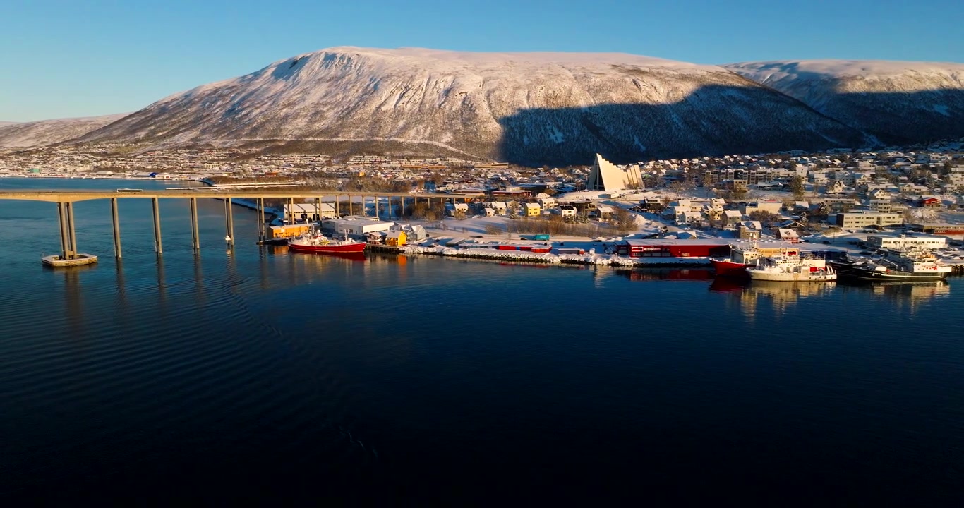 Vue aérienne de la ville enneigée de Tromsø et de la Cathédrale arctique illuminées par la lumière du soleil.