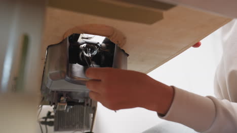 under table view of industrial singer sewing machine as garment maker adjusts internal mechanism, focusing on exposed metal components with partial view of person working beneath wooden surface