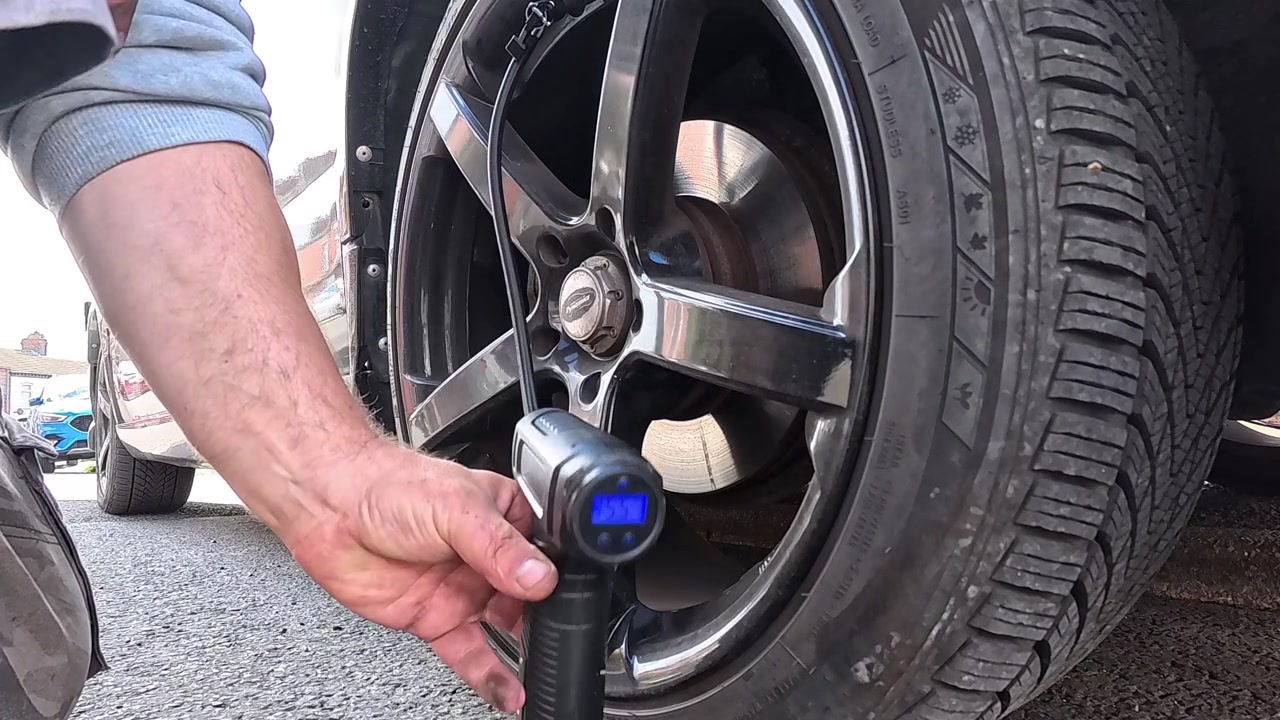 Man holding cordless portable air pump to inflate van tyre and checking the pressure