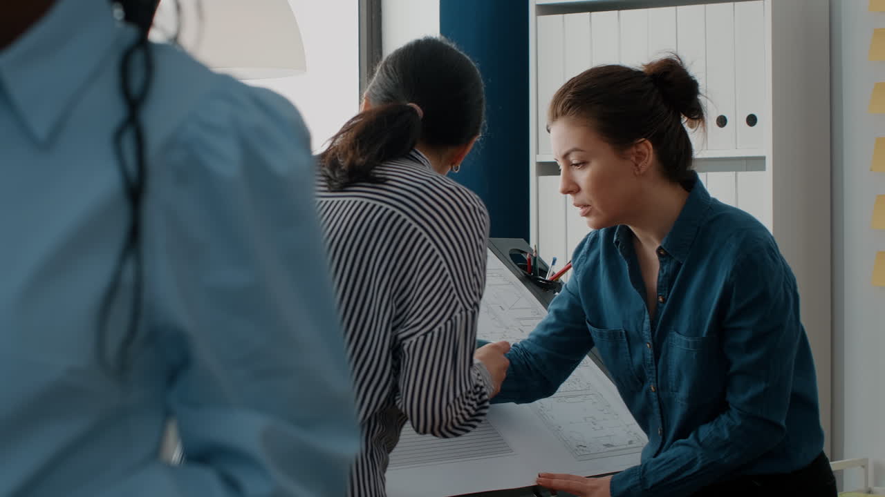 Architectural design office scene with women discussing blueprint details