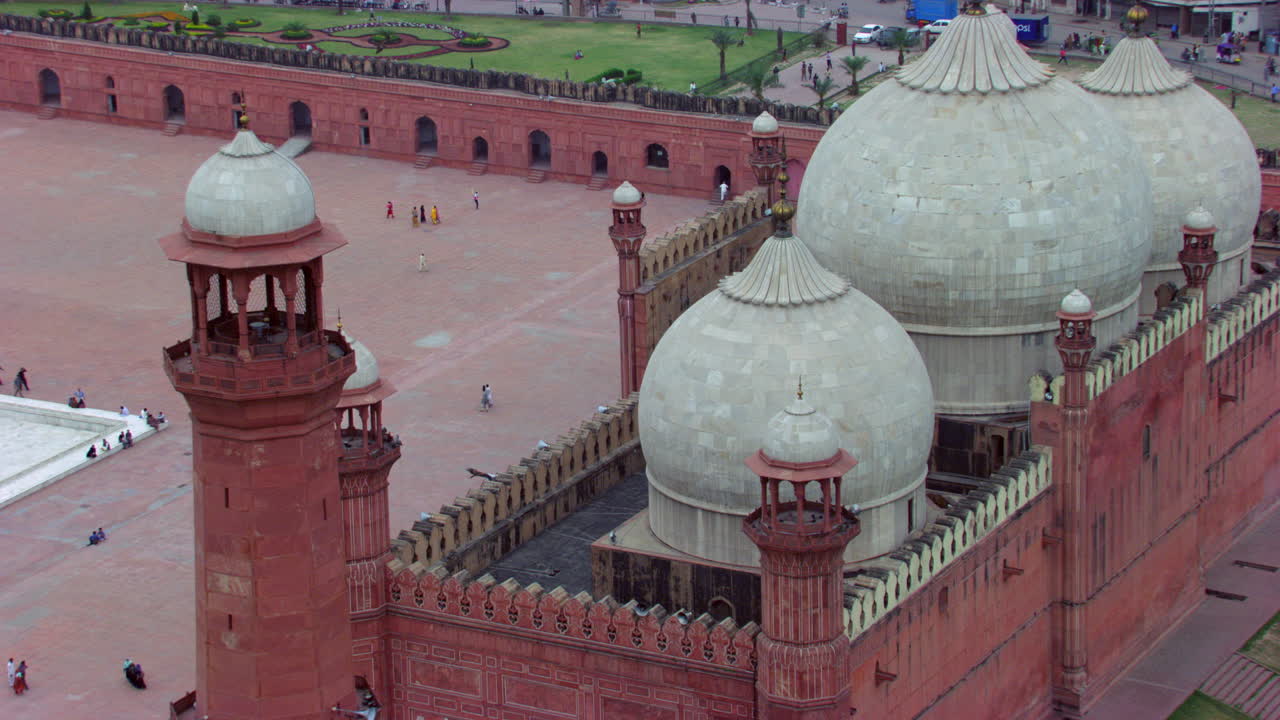 Lahore, Pakistán. Vista de cerca del suelo y los minaretes de la mundialmente famosa Mezquita Badshahi. Visitantes, damas, caballeros y niños en la Mezquita. Fieles en el patio de la Mezquita, milanos negros