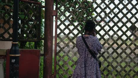 A-young-female-photographer-in-casual-summer-clothes-looking-away-while-standing-behind-a-fence-with-the-camera-during-a-trip-and-taking-photos