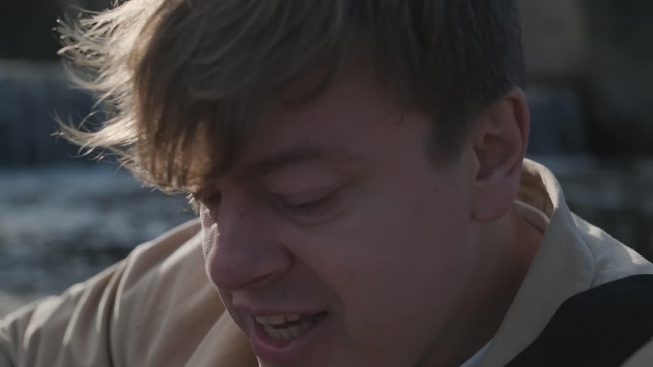 바위의 배경에 산의 강변에 앉아 기타를 연주하는 젊은이. 자유의 개념, 휴식 장소.