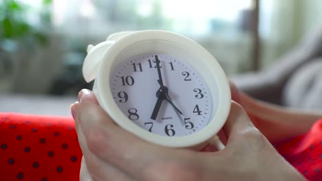 la mujer fija la hora en el despertador a las 6 y fija la alarma para la mañana.