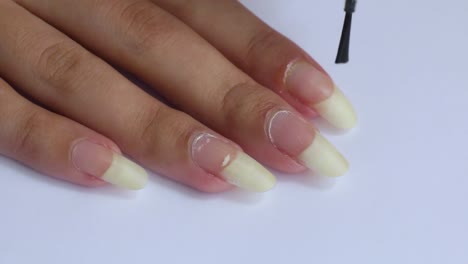 applying jojoba oil to cuticles on a female hand with long natural nails