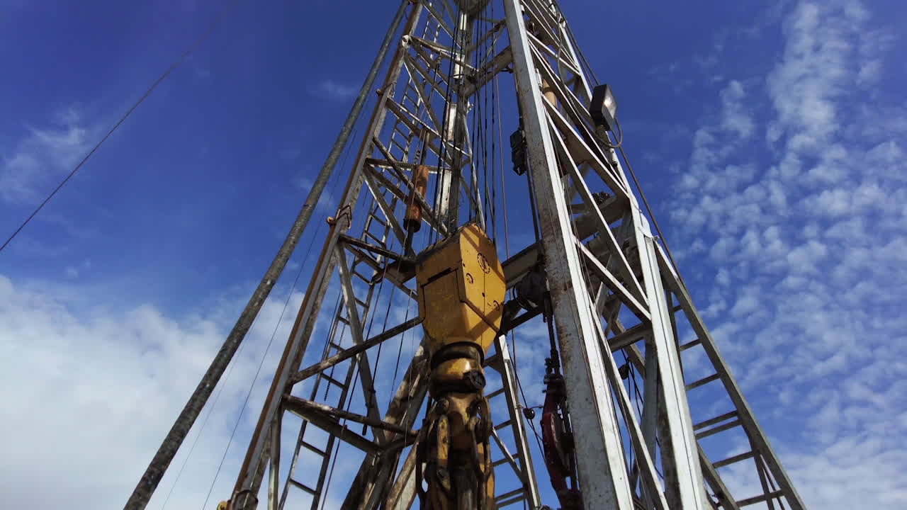 Drilling natural resources at the site for oil production. High metal derrick with equipment working. Low angle view.