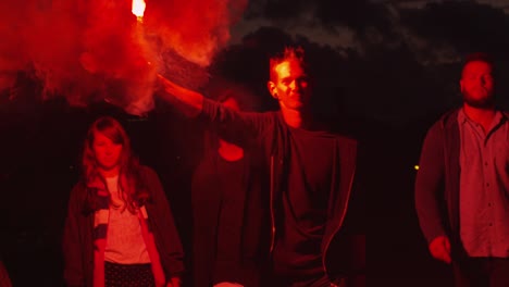 group of serious teenagers with one holding and waving red signal flare walking forward towards camera at night.