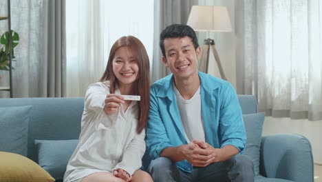 happy asian couple smiling to camera after find out positive pregnancy test in living room at home