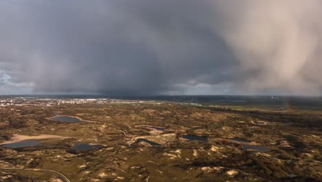 an aerial shot of the sand dunes in south holland province with dark clouds and heavy rainfall at the sea