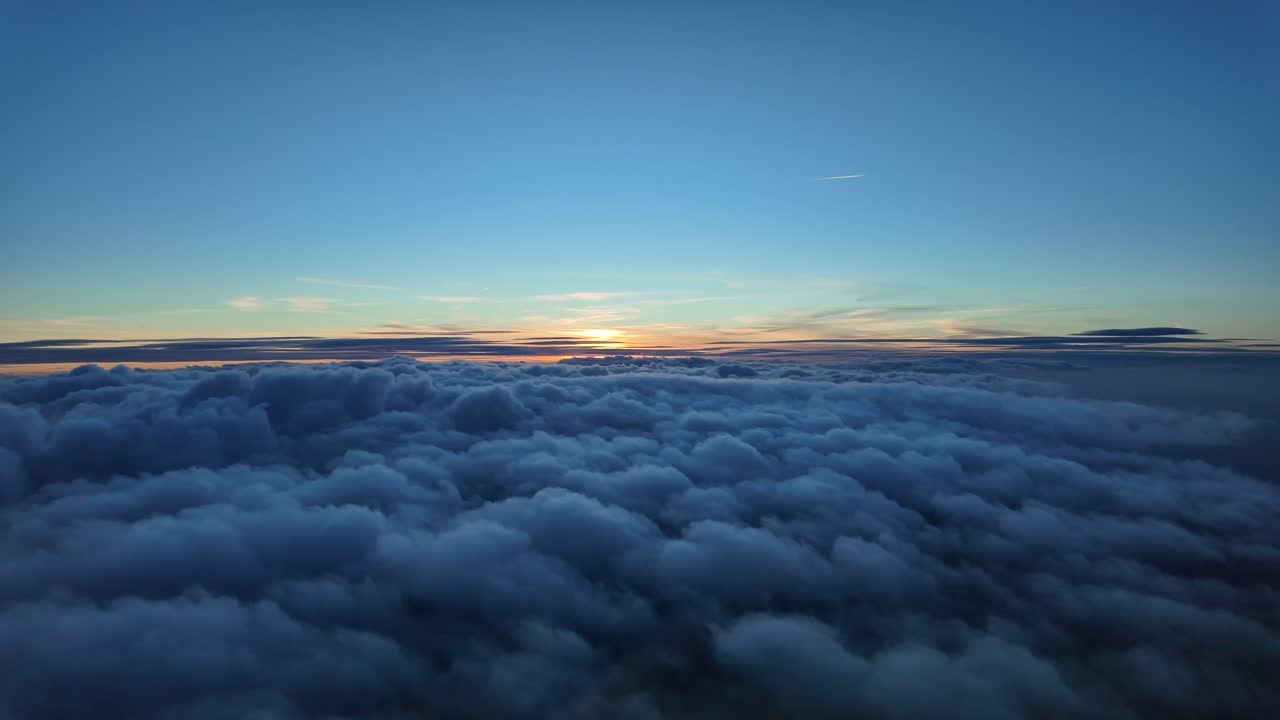 Immersive pilot POV of a twilight scene while flying over an endless blanket of stratus clouds and the sun sinking beyong a golden horizon