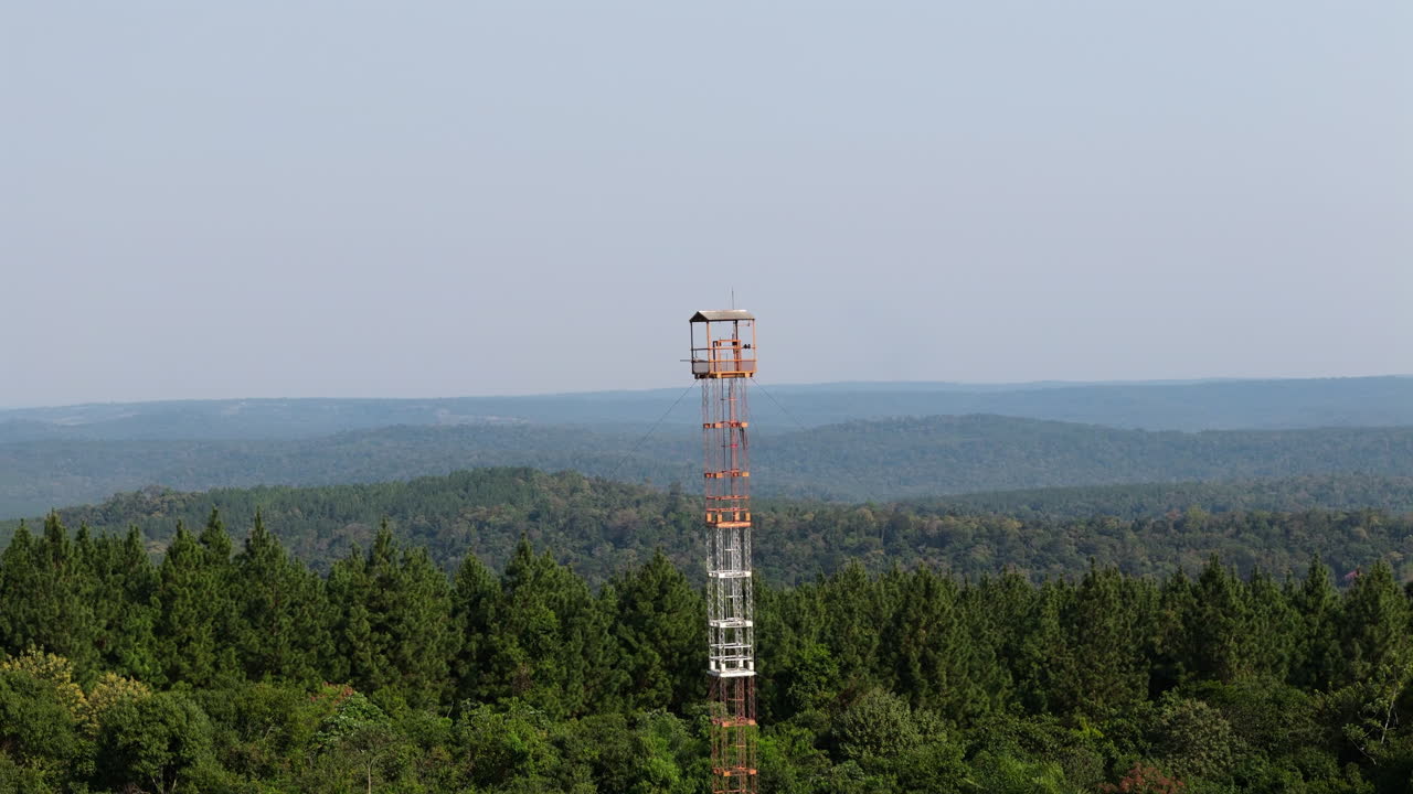 Forest fire lookout tower standing amidst dense forest canopy, aerial orbit of rural monitoring