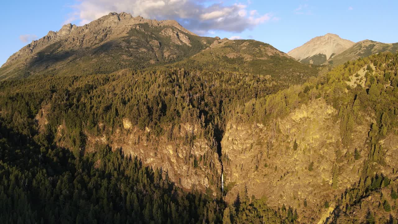 dolly aéreo sobre corbata blanca cascada de deshielo escondida entre las montañas del bosque de pinos al atardecer, patagonia argentina