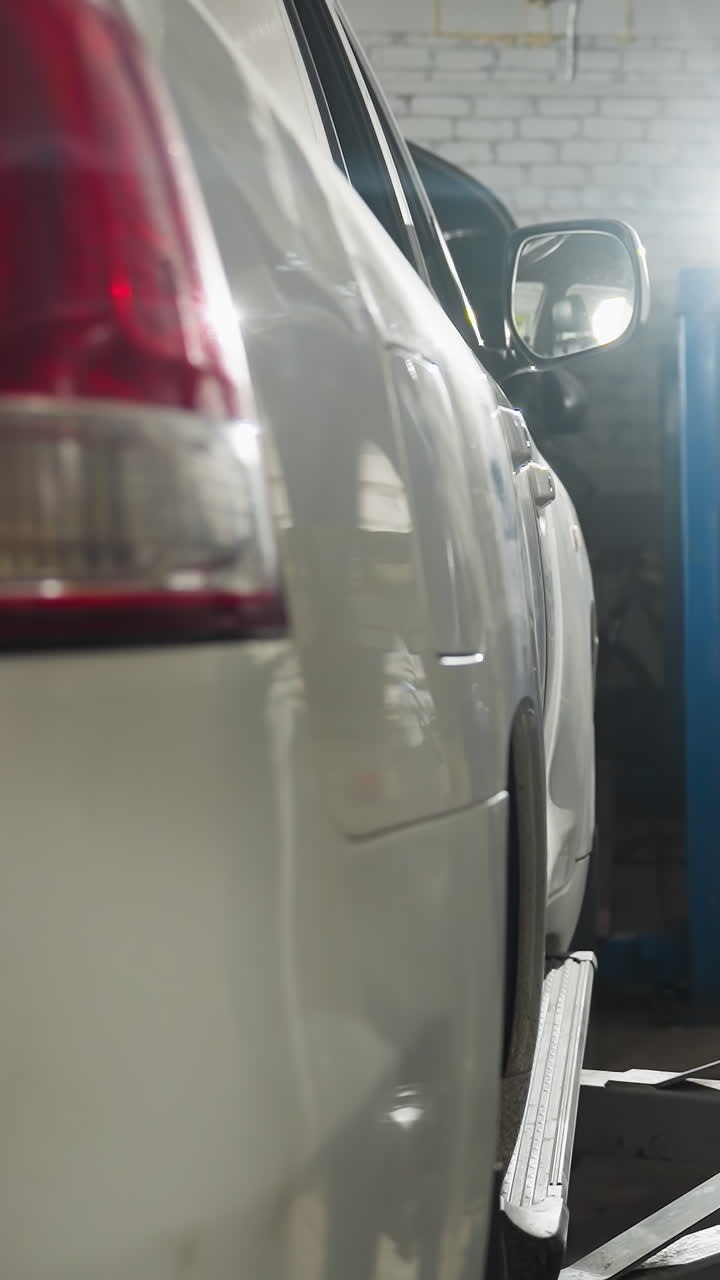 Un meccanico in uniforme blu preme il comando del sollevatore per alzare un'auto sullo sfondo di un'officina; la luce esalta la profondità e l'attività nell'area di lavoro.