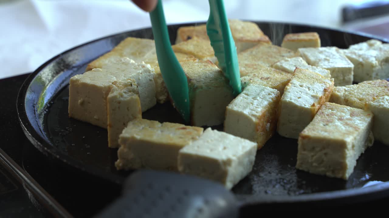 Tofu being flipped in cast iron pan special ingredients to cook a meal two cans of beans rice plantain avocado red onion and cilantro