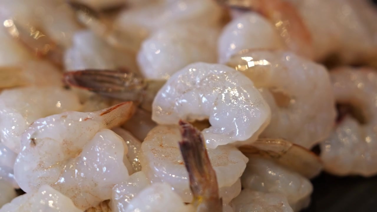 Primo piano di molti gamberi freschi crudi disposti ordinatamente su un vassoio da portata, che mostrano gusci traslucidi, texture naturale e qualità premium dei frutti di mare.