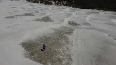 Drone-shot-of-a-man-walking-on-some-small-sand-dunes-on-Nye-Beach-in-the-coastal-town-of-Newport,-Oregon