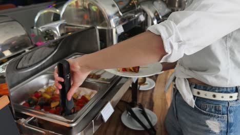 mujer que se sirve a sí misma de una línea de buffet con pinzas a la parrilla