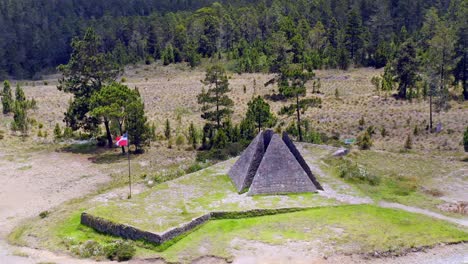 aerial orbit shot of colossal pyramid, valle nuevo and waving flag surrounded by forest in dominican republic